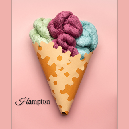 A paper cone holds three hanks of Hampton yarn, a Cascade Yarns premium yarn blend, against a pink background.