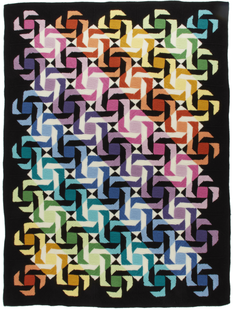 A multicolored knitted blanket, featuring geometric shapes. The Pinwheels Blanket, is a design by Margaret Holzmann.