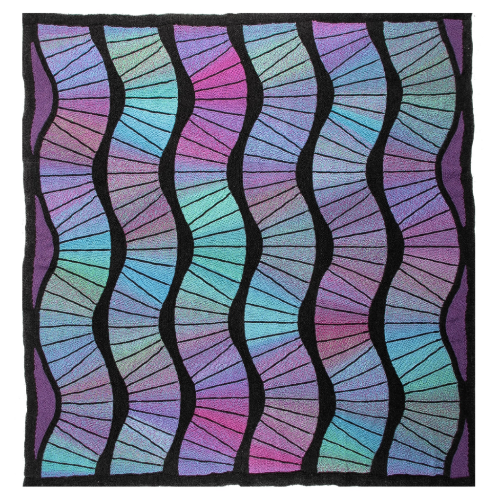A knitted teal, black, and blue blanket featuring geometric shapes. The Waves Blanket is a design by Margaret Holzmann.