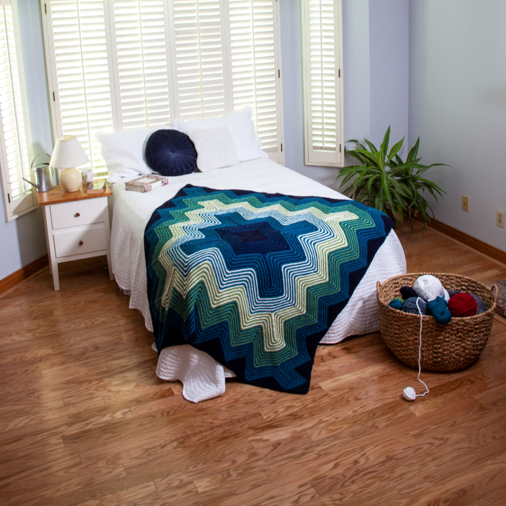 A knitted blanket is the focal point in a contemporary bedroom scene. The Pulsar blanket is a design by Margaret Holzmann.