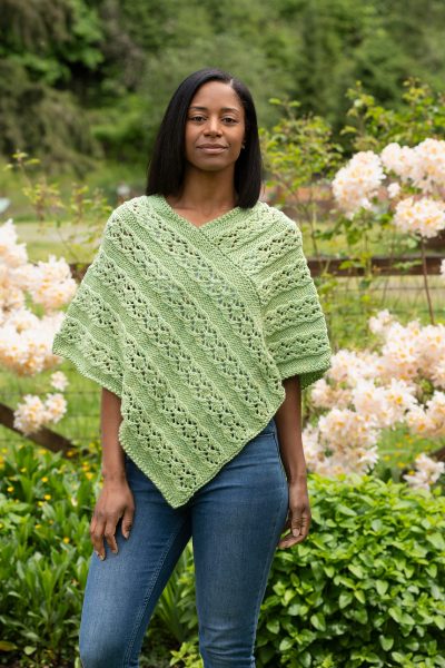 A person wearing a light green poncho is standing outside. The Lacy Diamond Poncho designed by Jennifer Kent is a free Cascade Yarns pattern.