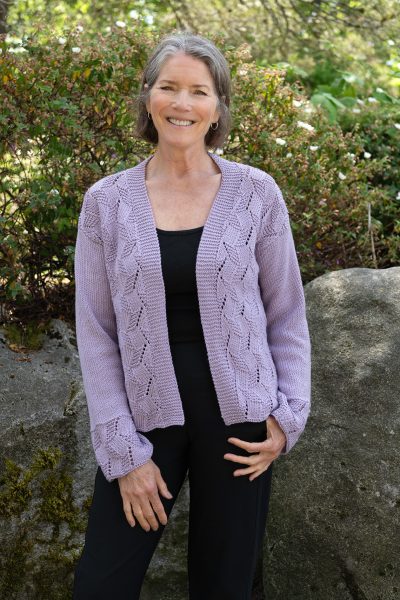 A person is standing outside wearing a purple cardigan. The Trellis Cardigan by Jennifer Kent is a free Casacde Yarns pattern.