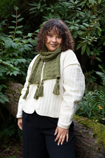 A person standing outside wearing a white jacket and a green scarf. The Both Sides Scarf designed by Jennifer Kent is a free Cascade Yarns pattern.